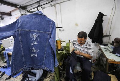 A Palestinian worker sews denim jackets for the Palestinian feminist fashion label "BabyFist", by designer Yasmeen Mjalli, in a workshop in Gaza City on November 27, 2018, with one of the jackets hanging nearby carrying writing on the back reading "fly" (beneath a butterfly) and "sting" (beneath a wasp). It's only three words on a T-shirt or embroidered on a denim jacket, but they carry a powerful message: "Not your habibti (darling)." "BabyFist" label founder Yasmeen Mjalli, 22, sees the clothes helping to empower Palestinian women facing unwelcome male attention in public, placing on the fabrics of muted colours and on canvas bags messages in English and Arabic inside drawings of flowers and other designs. / AFP / MAHMUD HAMS
