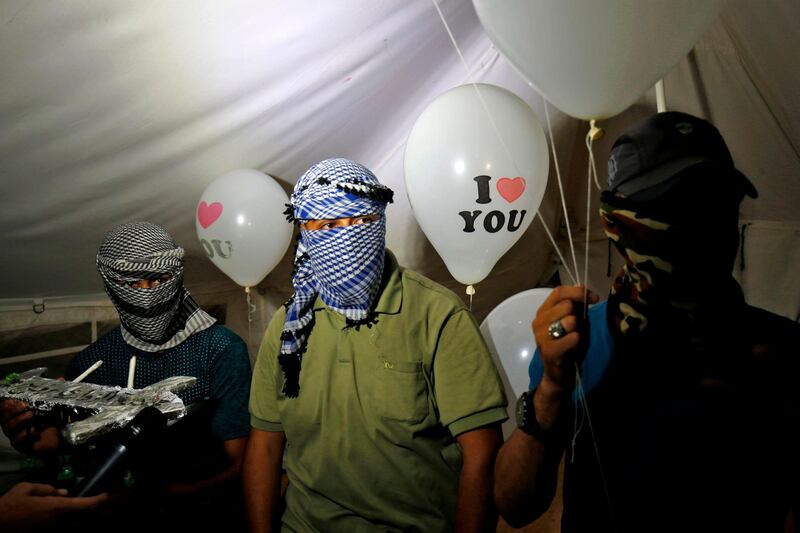 Masked Palestinian protesters calling themselves the "night confusion units" hold incendiary devices attached to ballons to be flown towards Israel, near the  Gaza-Israel border east of Rafah in the southern Gaza Strip, on September 26, 2018. The border protests since March 30 have been labelled the "Great March of Return" because they call for Palestinian refugees to return to their former homes inside what is now Israel. Hundreds of thousands of dollars in damage were caused to Israeli land -- including incinerated crops -- by the kites and balloons, Israeli authorities said. / AFP / SAID KHATIB
