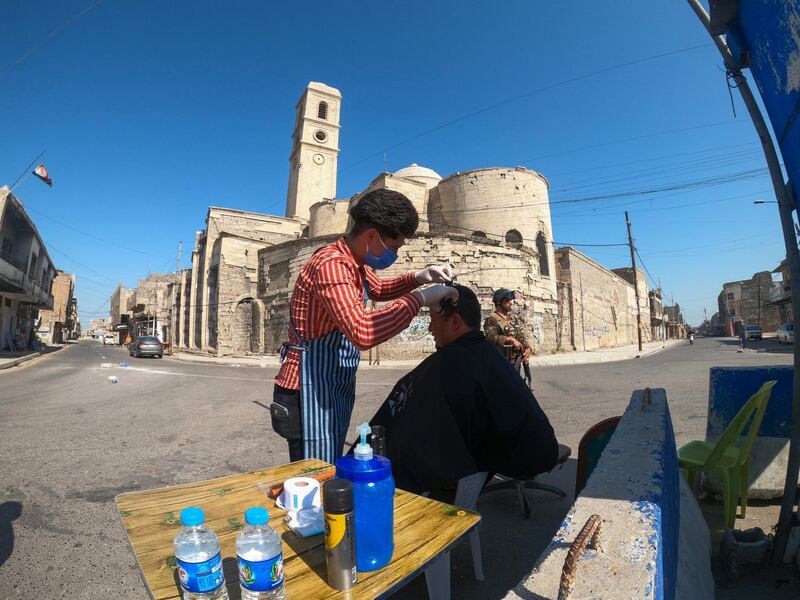 A barber wearing a protective face mask and gloves cuts the hair of a policeman, following the outbreak of the coronavirus disease (COVID-19), near the old bridge in the old city of Mosul, Iraq April 18, 2020. Picture taken April 18, 2020. REUTERS/Abdullah Rashid