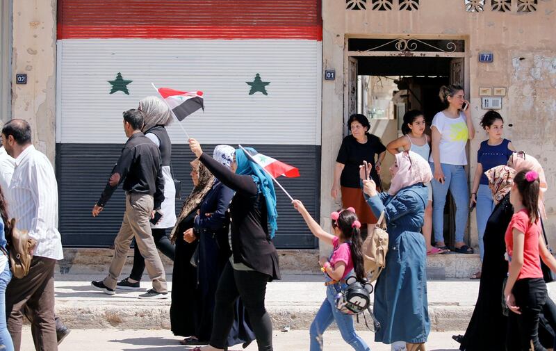 Returning Syrians walk together and hold flags as they enter the city of Qusayr. Reuters