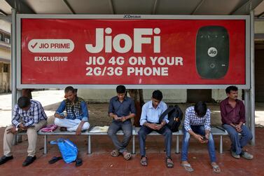 People wait at a bus stop advertising Jio's wireless network services for mobile phones. Qualcomm's investment values Jio Platform’s equity at about $65.3bn. Reuters