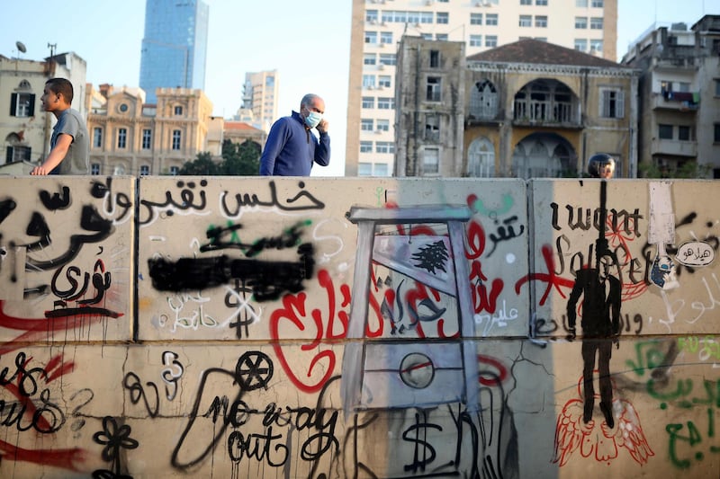 Lebanese protesters walk past a wall bearing graffiti of a hanging politician and a guillotine during a demonstration in the capital Beirut.   AFP