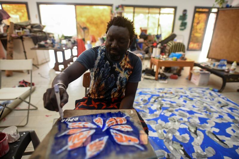 Senegalese artist Omar Ba signs his name on a painting of orange leaves in his studio in Bambilor, Senegal. Cooper Inveen / Reuters