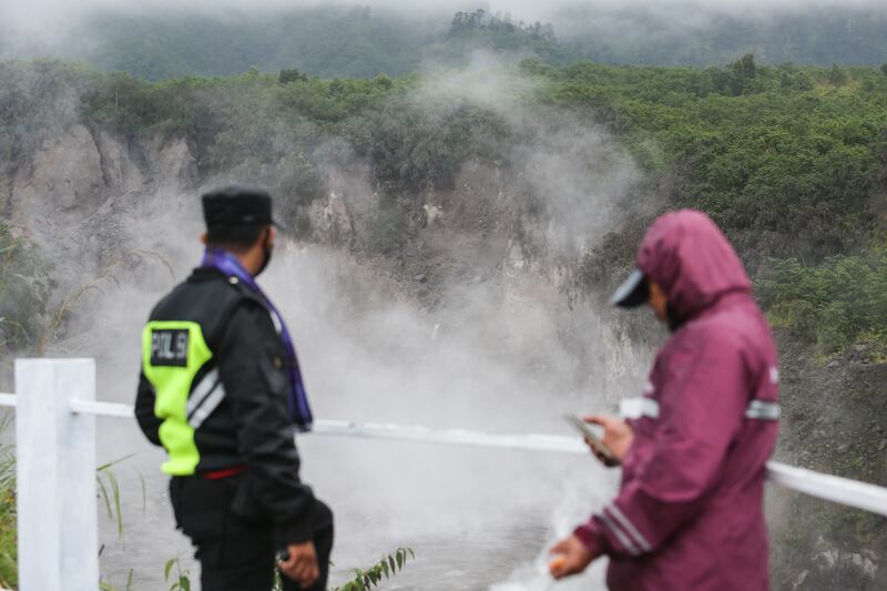 A police officer and a resident watch the hot lava flow into the Gendol river. Reuters