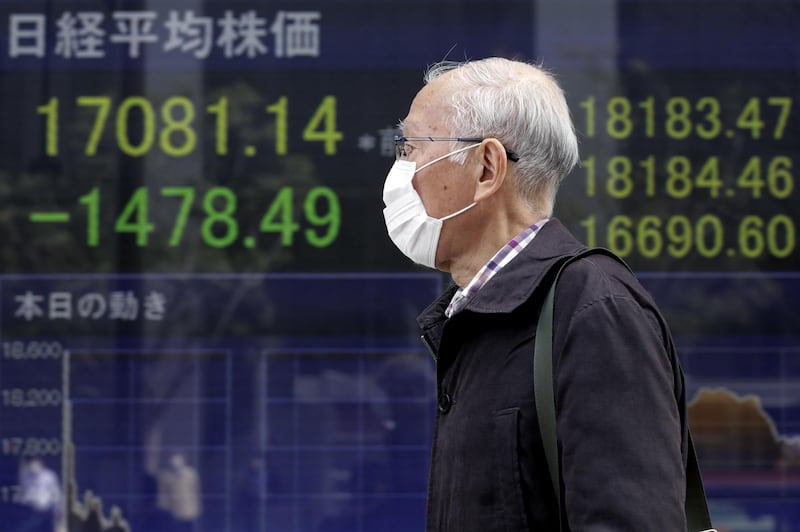 A pedestrian wearing a protective mask walks past an electronic stock board outside a securities firm in Tokyo, Japan. Bloomberg