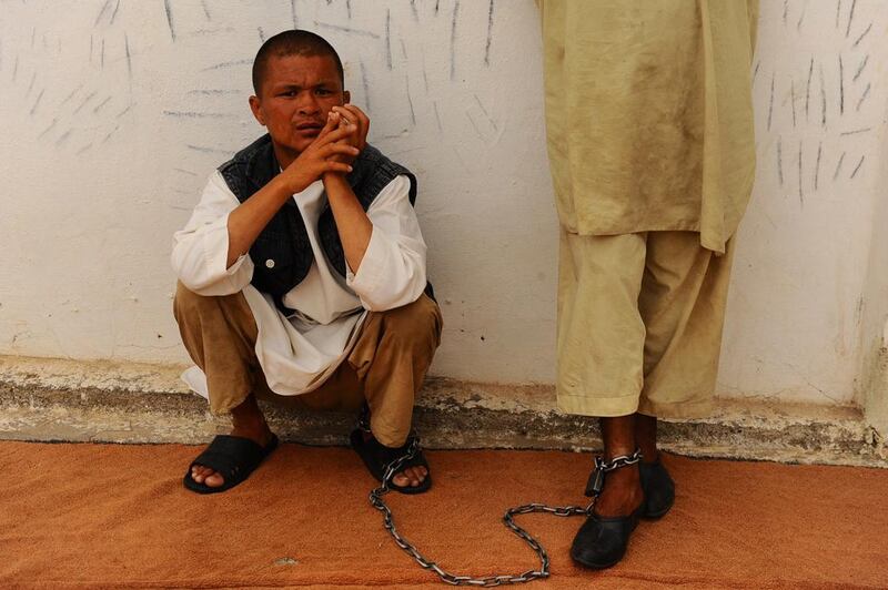 An Afghan patient squats against a wall chained to another patient for security purposes.