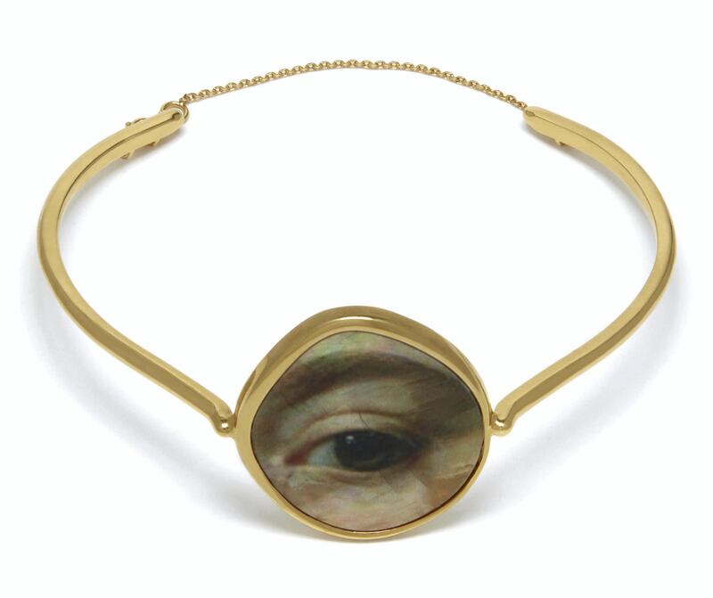 A minimalist gold bangle is decorated with a close-up image of an eye and eyebrow