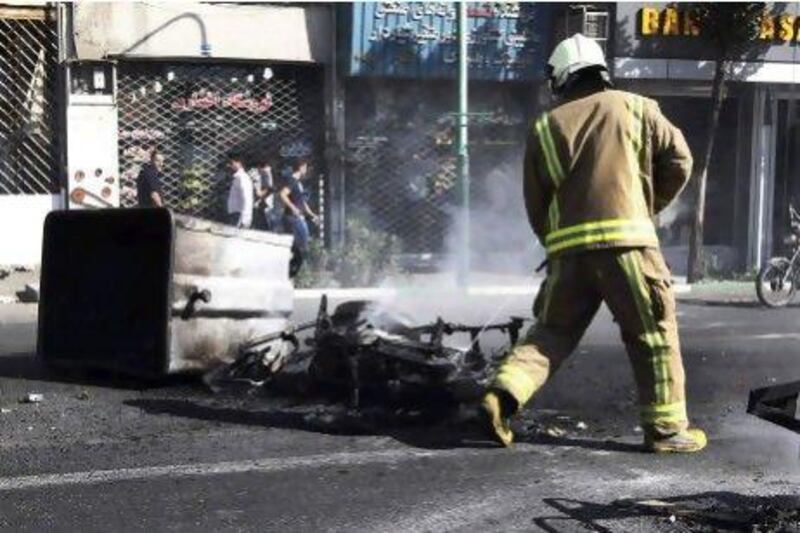 An Iranian fireman extinguishes a burned motorcycle in a street in central Tehran, near the main bazaar, yesterday. Police threatened merchants who closed their shops in the bazaar as part of a push to halt the plunge of the rial.