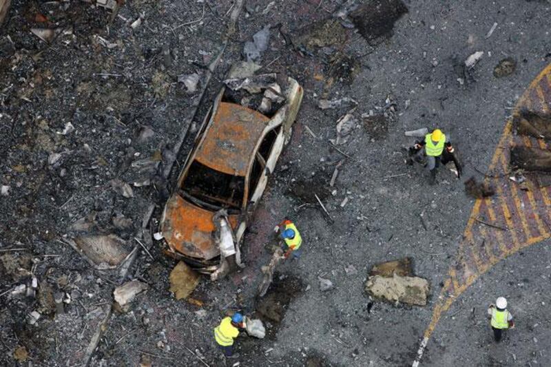 Workers remove debris near a burnt out car outside Tamweel Tower.