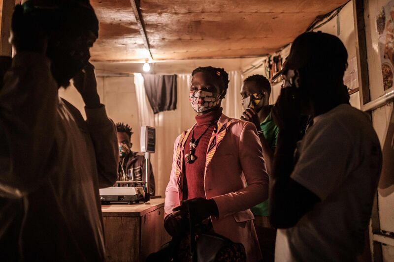 This picture taken on March 23, 2020 shows Lookslikeavido fashion designer David Avido (C), 24, who makes face masks from remnants of cloth he uses and distributes them to the public for free almost everyday, giving his handmade face masks to people at a butcher shop in Kibera as a preventive measure against the spread of the COVID-19 novel coronavirus.  / AFP / Yasuyoshi CHIBA
