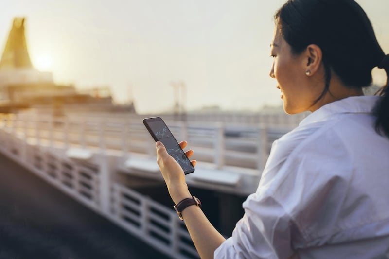 Busy businesswoman checking financial trading data on smartphone in commercial dock in city during sunset