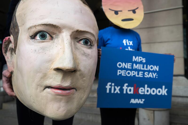 A demonstrator holds a mask depicting Facebook chief executive Mark Zuckerberg, left, as he stands with a demonstrator wearing an angry emoji mask outside the venue of a UK parliamentary committee hearing in London. Simon Dawson / Bloomberg