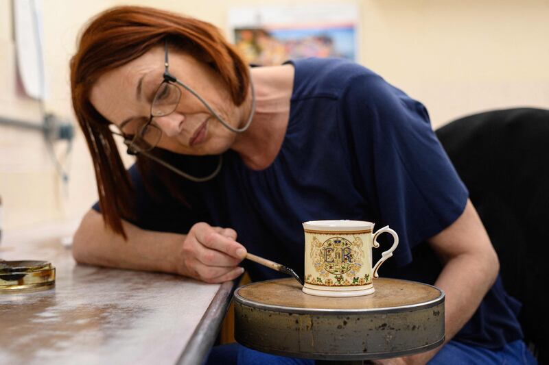 Gilder Claire Wright applies gold paint by hand as she works to produce a platinum jubilee commemorative beaker for Goviers, as part of its Royal Commemoratives collection. AFP