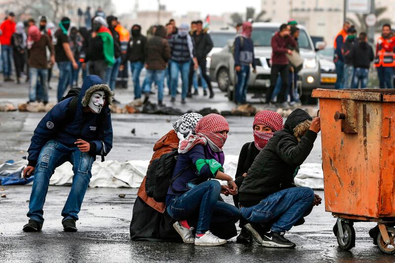 Palestinian girls with their faces covered with traditional chequered keffiyehs hide behind a bin during clashes with Israeli forces following a demonstration marking "Land Day". AFP