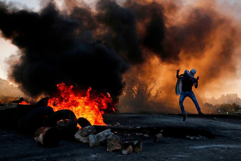 A Palestinian uses a slingshot to hurl stones amid smoke during clashes with Israeli troops in Ramallah. AFP