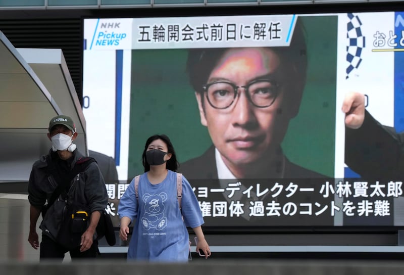 Pedestrians walk past a huge display showing news report about the Tokyo 2020 Organising Committee sacking of Opening Ceremony director Kentaro Kobayashi, after footage from the late 1990s recently emerged of a skit in which he appears making jokes about the Holocaust.