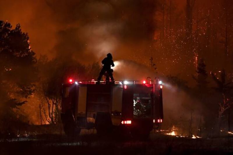 A firefighter douses flames from the top of a truck as a fire spreads around the village of Afidnes, some 30 kilometres north of Athens. AFP