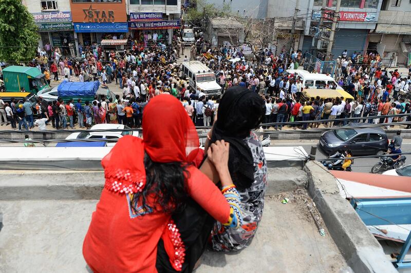 Women sitting on a rooftop watch as bystanders gather while an ambulance carrying bodies of victims drives out near the site where 11 family members were found dead inside their home in the neighbourhood of Burari in New Delhi on July 1, 2018.   Police have cordoned off the home in Burari in the north of the capital where the bodies of seven women and four men were discovered July 1. "10 of the 11 family members were found hanging when we reached the house. The last, a 75-year-old female, was dead on the floor," a Delhi police official told AFP. / AFP / Sajjad HUSSAIN
