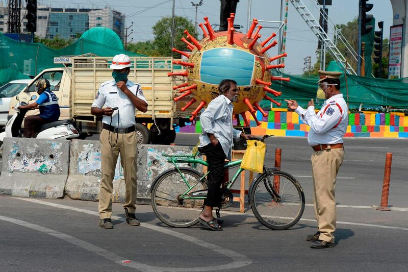 A traffic officer (R) gestures as he asks to a man to wear a facemask near a coronavirus-themed globe at a traffic junction during a government-imposed nationwide lockdown as a preventive measure against the COVID-19 coronavirus, in Hyderabad, on April 18, 2020. / AFP / NOAH SEELAM
