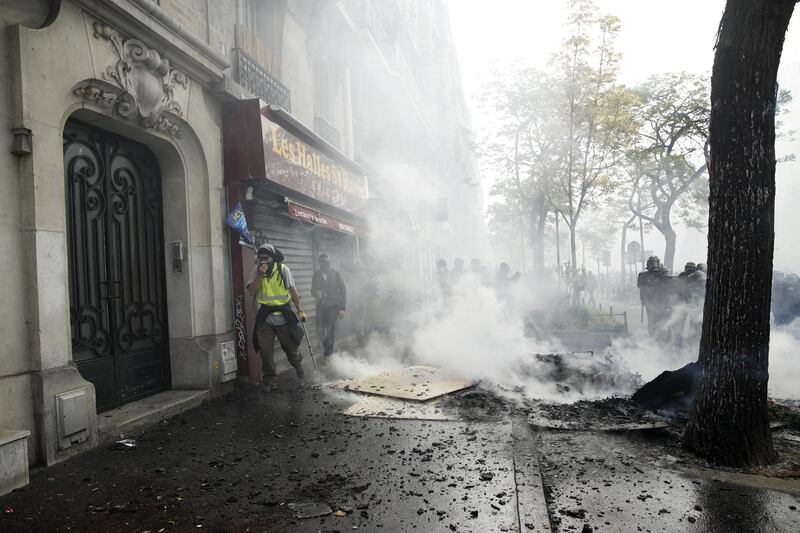 A Yellow Vest protester walks by a building through smoke during a demonstration of the French trade unions members and the Gilets Jaunes movement marking Labor Day in Paris. EPA