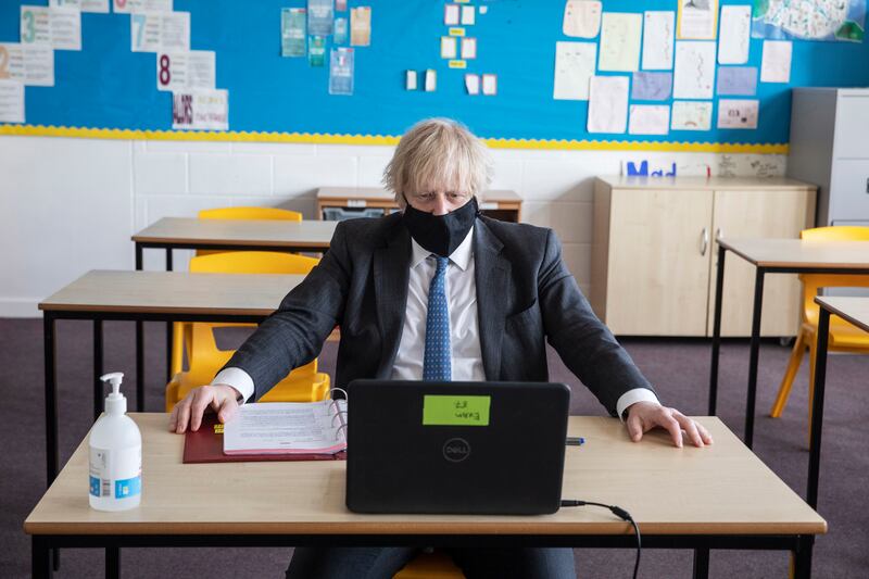 UK Prime Minister Boris Johnson sits at a desk in a school classroom in England, where air quality monitors will be fitted in the new term. Getty