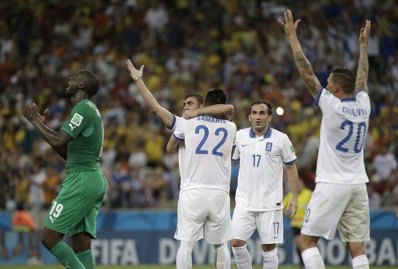 Yaya Toure reacts as Greek players celebrate after their 2-1 victory over Ivory Coast in Fortaleza. Bernat Armangue / AP Photo