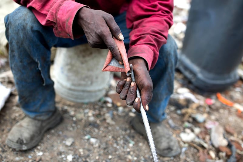 Mr Aristide, a 36-year-old trash scavenger, uses sand paper to smoothen the metal rod he uses to pick through the rubble. AP Photo