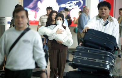 HONG KONG - MARCH 17:  A mother wears a face mask as she carries her baby into Hong Kong's Chek lap Kok airport to protect herself from a flu-like virus that's hit the region March 17, 2003 in Hong Kong. Airports checked passengers for symptoms as a deadly and contagious respiratory virus has killed one person, a 50-year-old American businessman, and infected over 150 people, including medical personnel throughout Honk Kong hospitals. The World Health Organization (WHO) has sent a global alert after flu outbreaks in Hanoi and Hong Kong and has collected samples from patients to see if a virus or bacteria is causing the mystery illness. The WHO has issued a warning to people who have traveled to Hong Kong to seek medical help if they come down with flu like symptoms. (Photo by Christian Keenan/Getty Images)