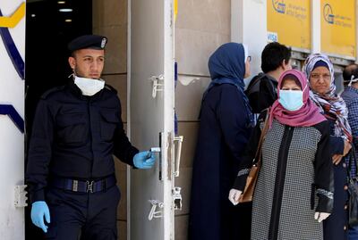 FILE PHOTO: A Palestinian policeman stands guard as a woman, wearing a mask as a precaution against the the coronavirus disease (COVID-19), waits with other people outside a bank to withdraw cash, in Gaza City March 29, 2020. REUTERS/Mohammed Salem/File Photo