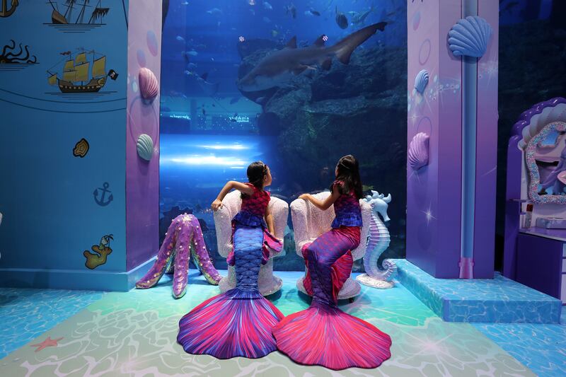 The siblings in their mermaid costumes gaze into the depths of the aquarium