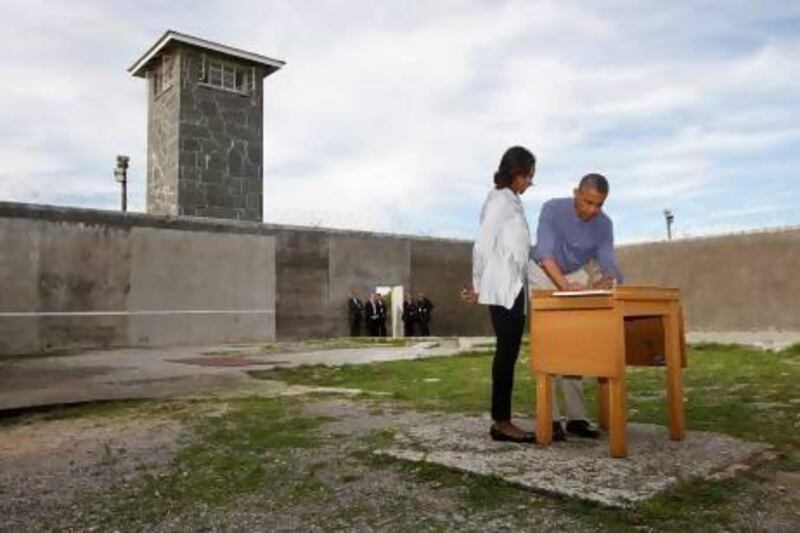 Barack Obama writes in a guest book as he tours Robben Island with first lady Michelle Obama.
