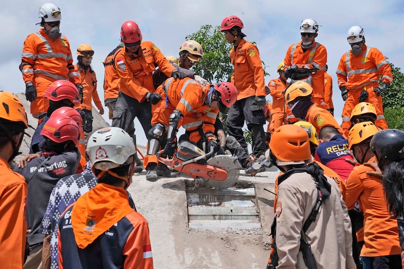 Rescuers use a saw as they try to recover the body of a victim from under the rubble of a collapsed building in Cianjur. AP