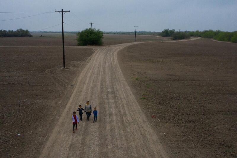 Sonia, an asylum-seeking migrant from Honduras, walks down a dirt road with her three children Jefferson, 9, Scarlet, 7, and David, 6, after they crossed the Rio Grande river into the United States from Mexico on a raft in Penitas, Texas, U.S., March 16, 2021. Picture taken with a drone. REUTERS/Adrees Latif