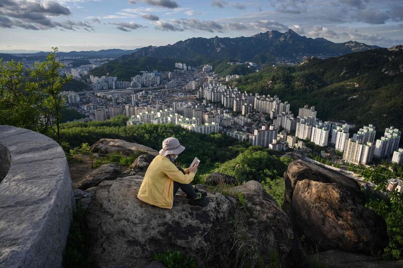 A photo taken on June 7, 2019 shows a woman looking at a phone before apartment buildings of the Seoul city skyline. AFP