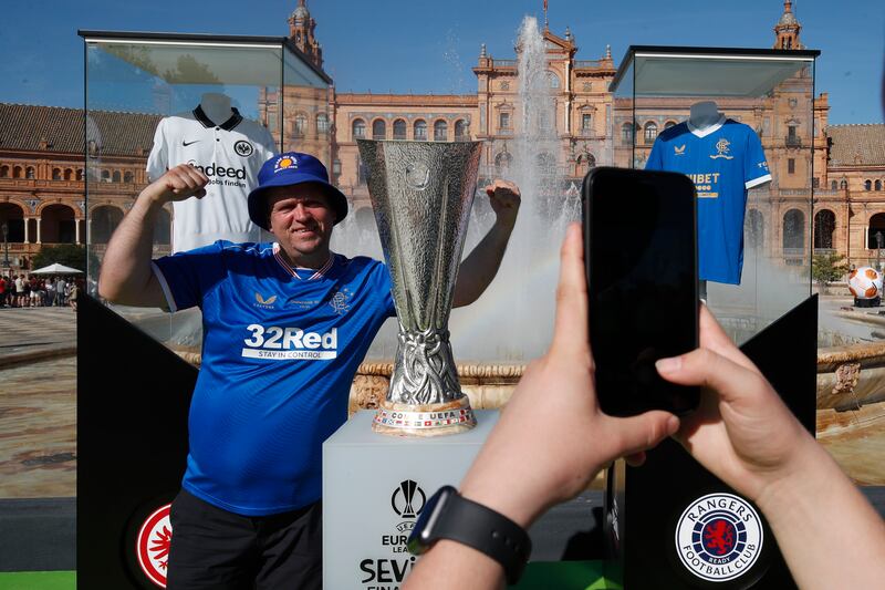 A Glasgow Ranger supporter poses for a photo next to a replica trophy in downtown Seville. AP