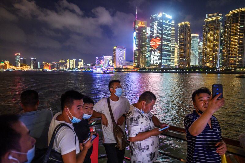 SHANGHAI, CHINA - SEPTEMBER 01: Chinese tourists, some wearing protective masks, take photos and stand on the deck of a tourist boat on the Huangpu River as the skyline of the Pudong district can be seen on September 1, 2020 in Shanghai, China. (Photo by Kevin Frayer/Getty Images)