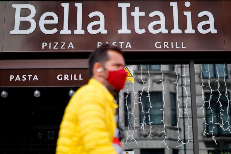 A pedestrian wearing a facemask walks past a Bella Italia restaurant in The Strand, central London on July 3, 2020. Casual Dining Group, owner of Bella Italia, Cafe Rouge and Las Iguanas, is to cut more than 1,900 jobs and close 91 restaurants after calling in administrators. / AFP / Tolga Akmen
