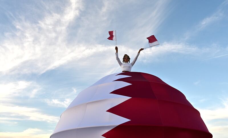A performer waves Qatari flags as she welcomes fans arriving at the match between the Netherlands and Qatar. EPA