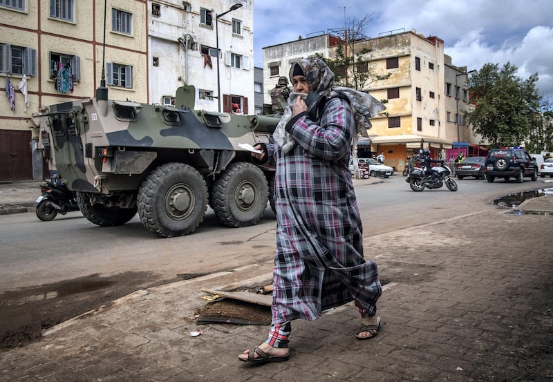 A woman walks past a Moroccan military armoured personnel carrier (APC) driving along a road, instructing people to remain at home, in the capital Rabat on March 22, 2020. - A public health state of emergency went into effect in the Muslim-majority country late on March 20, and security forces and the army have been deployed on the streets to combat the spread of COVID-19 coronavirus disease. People have been ordered to stay at home, and restrictions on public transport and travel between cities are also in place. (Photo by FADEL SENNA / AFP)
