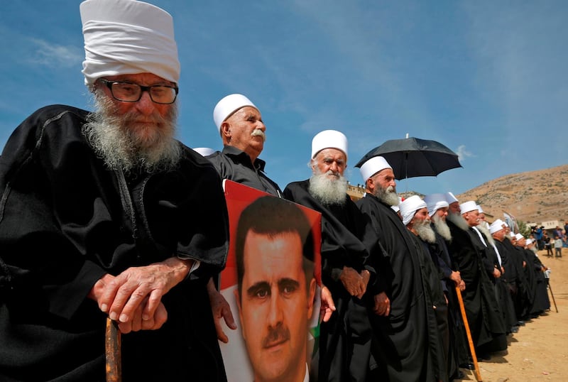 Elderly members of the Druze community stand holding a portrait of Syrian President Bashar al-Assad during a rally in the Druze village of Majdal Shams in the Israeli-annexed Golan Heights on October 6, 2018 commemorating the 45th anniversary of the 1973 Arab-Israeli war.  / AFP / JALAA MAREY
