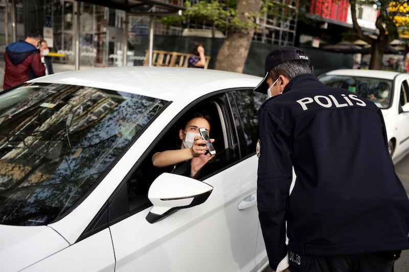 A police officer checks a person's ID at a checkpoint in a nearly deserted street in the city centre, in Ankara. AP