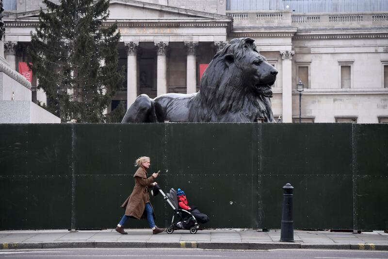 A woman pushes a child in a pushchair past Trafalgar Square. Getty Images