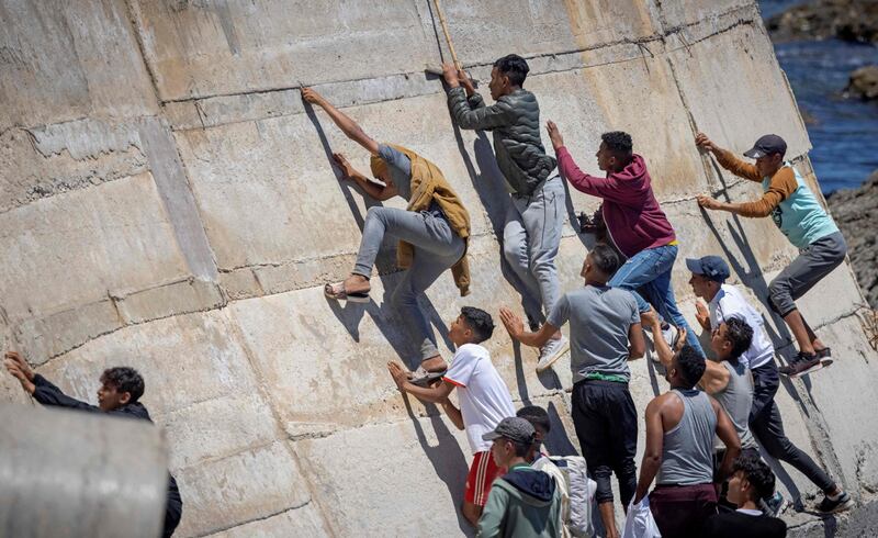 Migrants try to scramble up a wall separating the Spanish enclave of Ceuta from Morocco. A record 8,000 poured over the border this week, but many were swiftly returned. AFP