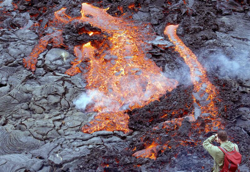 A man takes a picture as lava flows from the volcano. Now officially named Fagradalshraun, or 'beautiful valley of lava' after the nearby Mount Fagradalsfjall, the volcano rose up from a fissure in the ground. AFP