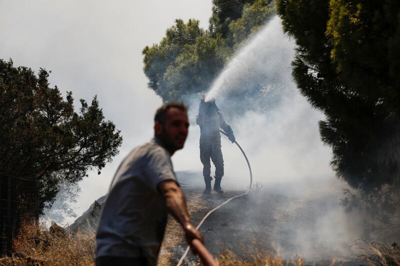 A man helps a firefighter while he tries to extinguish a wildfire burning in Markati.