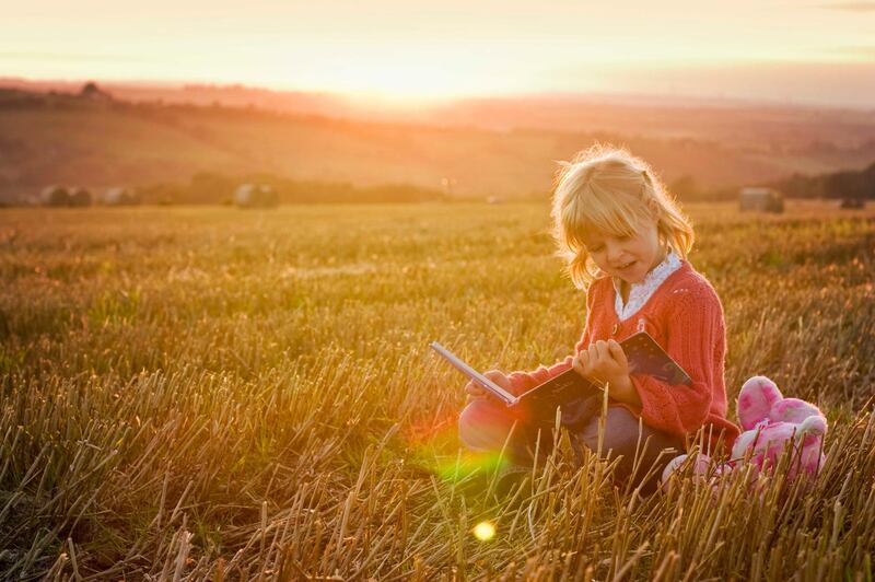 Little girl reading to her teddy outdoors near sun down in rural Scotland in late summer. Getty Images
