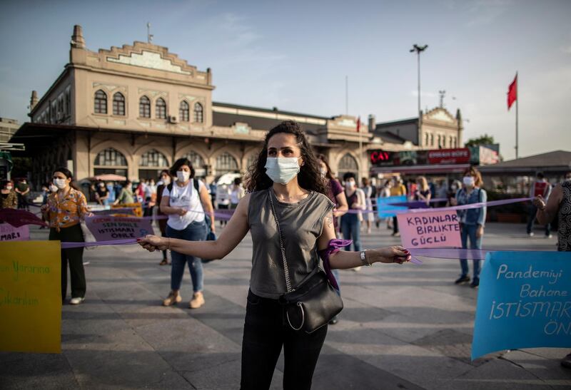 Protesters wearing protective face masks hold placards and shout slogans while maintaining social distance with purple ribbons due to the ongoing coronavirus pandemic during a protest against abuse of women and children in Istanbul, Turkey.  EPA