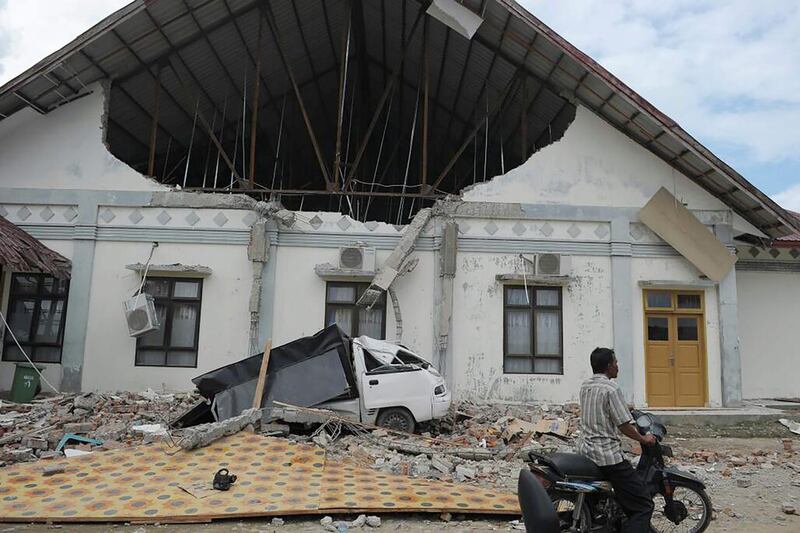 A man rides past a district hospital which was damaged after the earthquake in Pidie Jaya, Aceh province on December 7, 2016.  At least 52 people were killed and hundreds injured on December 7 after a strong earthquake struck Indonesia’s Aceh province, with officials warning the death toll would likely rise. Chaideer Mahyuddin / AFP