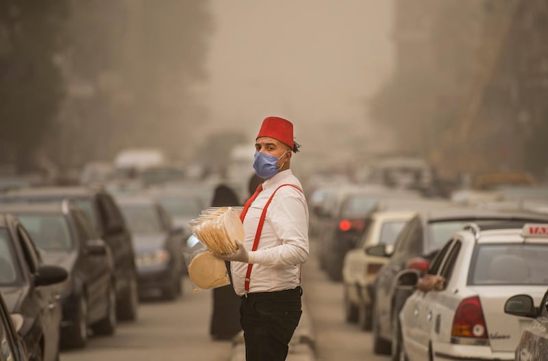A street vendor wearing protective face mask stands between lines of cars during a sandstorm in Cairo, Egypt.  EPA