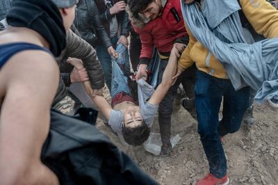 TOPSHOT - Migrants carry an injured man after Greek security officer shot him as they tried to pass on Greek side, near Pazarkule crossing gate in Edirne, Turkey,  on March 4, 2020.  Turkish officials claimed on March 4, 2020 that one migrant was killed by Greek fire on the Turkey-Greece border where thousands of migrants have massed since last week. But on the other side Greece "categorically" denied claims by Turkey that it had fired live bullets against migrants on the border, with several allegedly injured and one later dying. / AFP / BULENT KILIC
